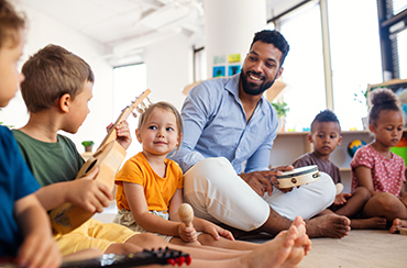 Image of an educator with a group of children sitting and playing musical instruments