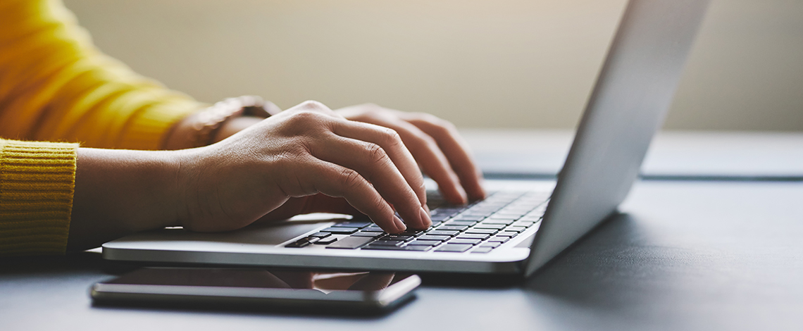 Woman’s hands typing on a laptop.