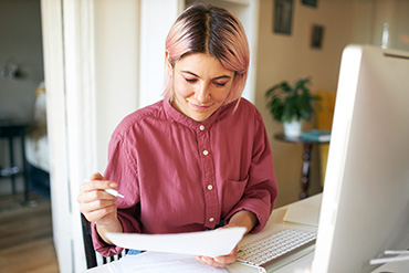 An individual reading a piece of paper while holding a pen.