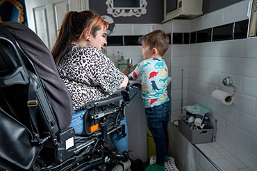 A woman, who is seated in a wheelchair, is helping a child wash his hands. 