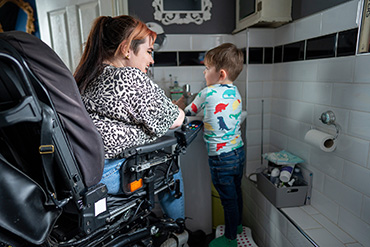 Une femme est assise dans un fauteuil roulant. Elle aide un enfant à se laver les mains.