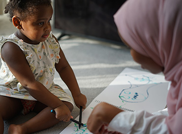 Un jeune enfant et une éducatrice de la petit enfance colorient.